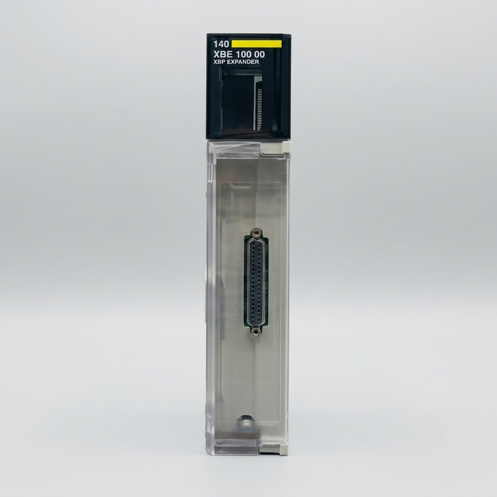 Front view of a Schneider Electric Modicon Quantum 140 XBE 100 00 backplane expander module on a plain gray background, with the diagnostics cover and deterministic networked multi-pin connector visible.
