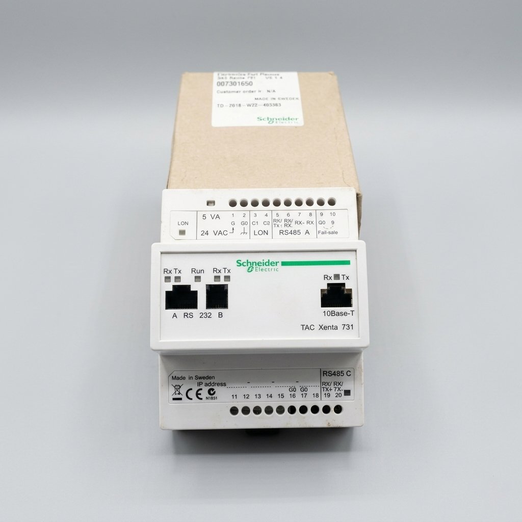 Front perspective view of a white Schneider Electric TAC Xenta 731 building automation controller with its original cardboard box, showing Ethernet, RS 232, and RS485 ports, terminal wiring labels, and status LEDs, against a clean light gray background.